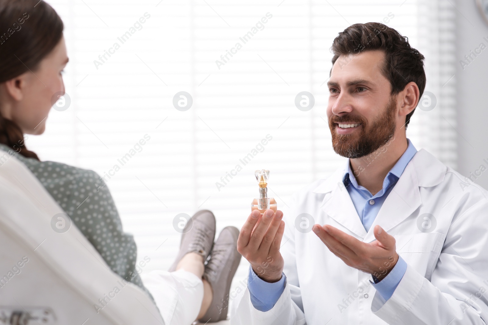 Photo of Doctor with educational model of dental implant consulting patient in clinic