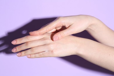 Photo of Woman applying cream on her hand against violet background, closeup