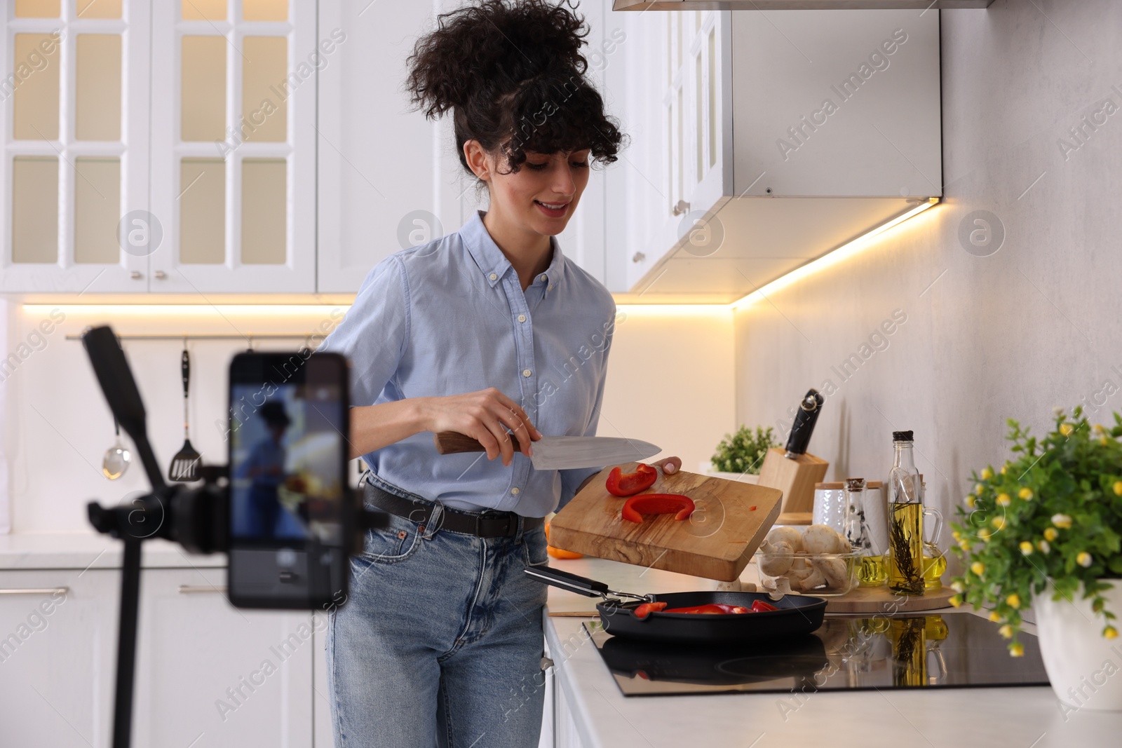 Photo of Smiling food blogger cooking while recording video in kitchen