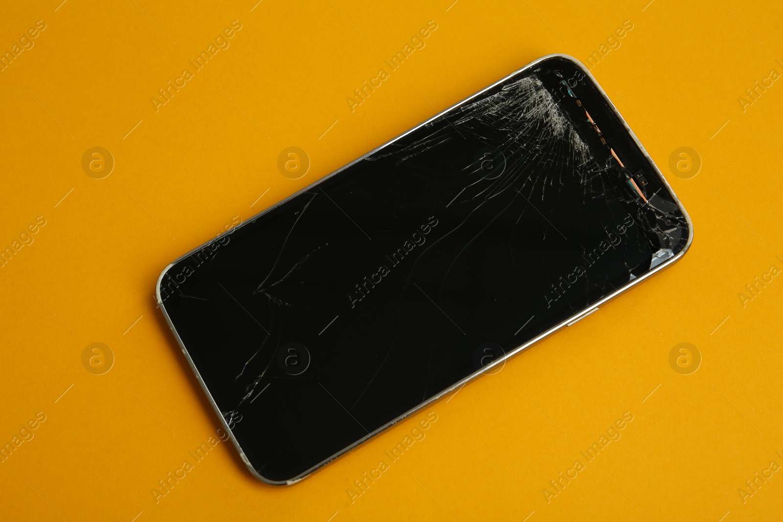 Photo of Smartphone with cracked screen on orange background, top view. Device repair