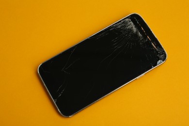 Photo of Smartphone with cracked screen on orange background, top view. Device repair
