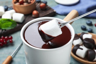 Photo of Dipping marshmallow into melted chocolate at blue wooden table, closeup