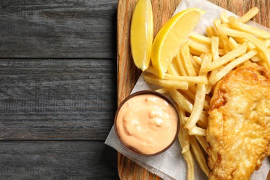 Photo of Board with British traditional fish and potato chips on wooden background, top view. Space for text