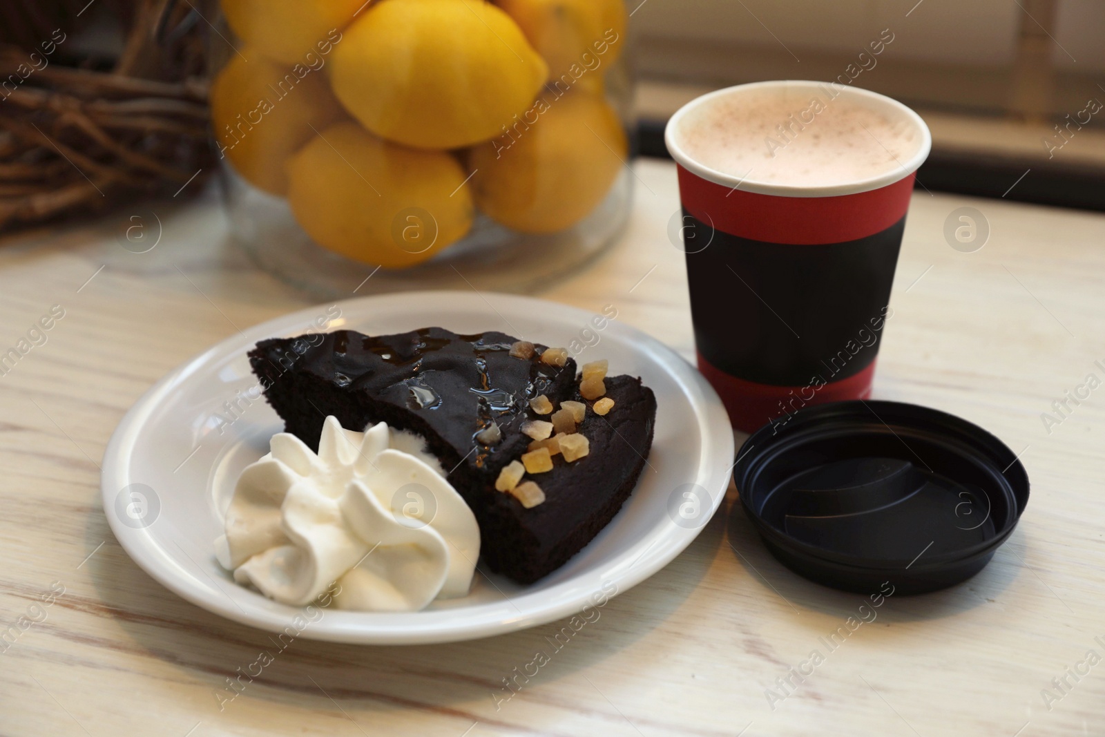 Photo of Tasty coffee in takeaway paper cup and dessert on wooden table indoors