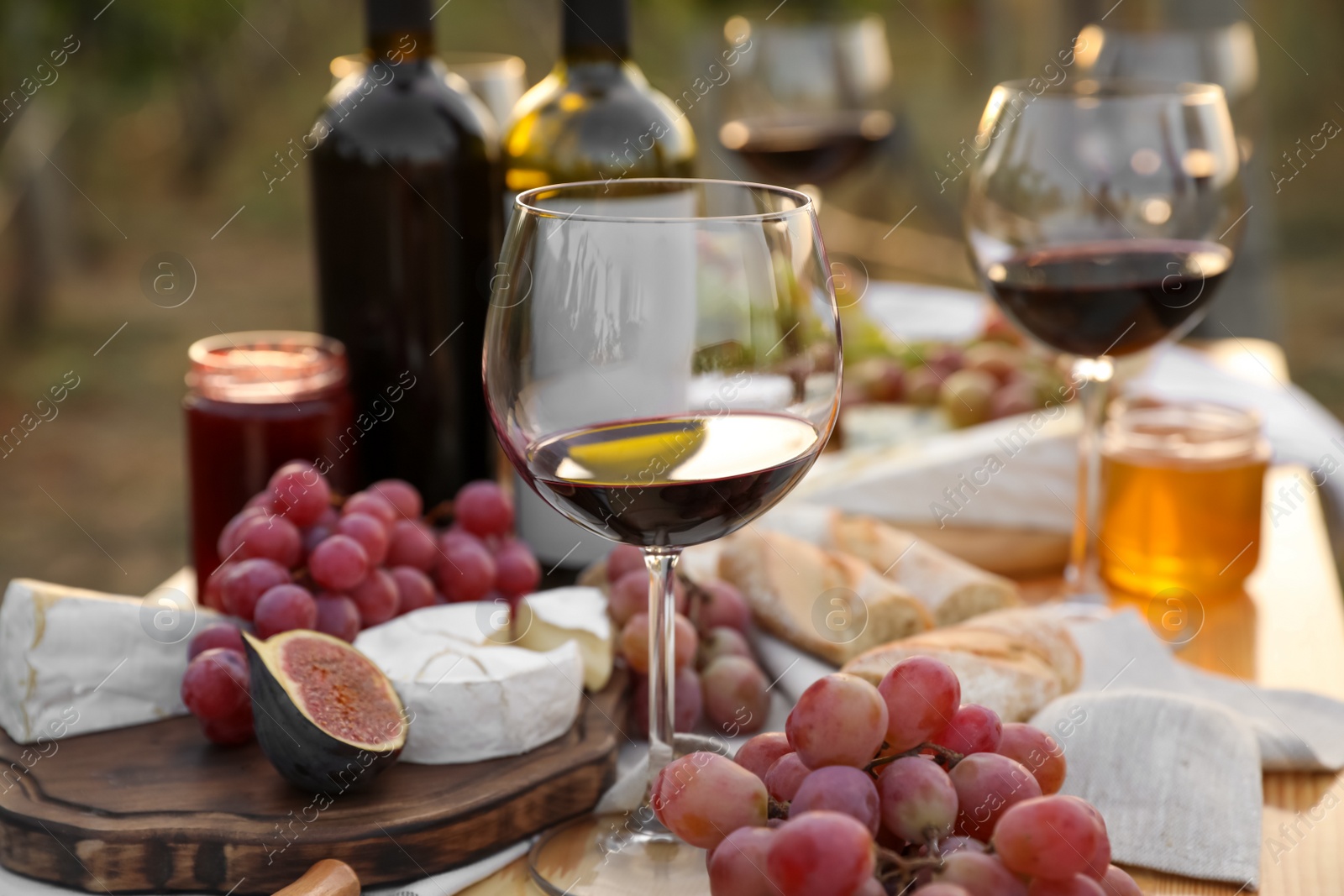 Photo of Red wine and snacks served for picnic on wooden table outdoors, closeup