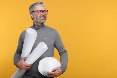 Photo of Architect with hard hat and drafts on orange background. Space for text