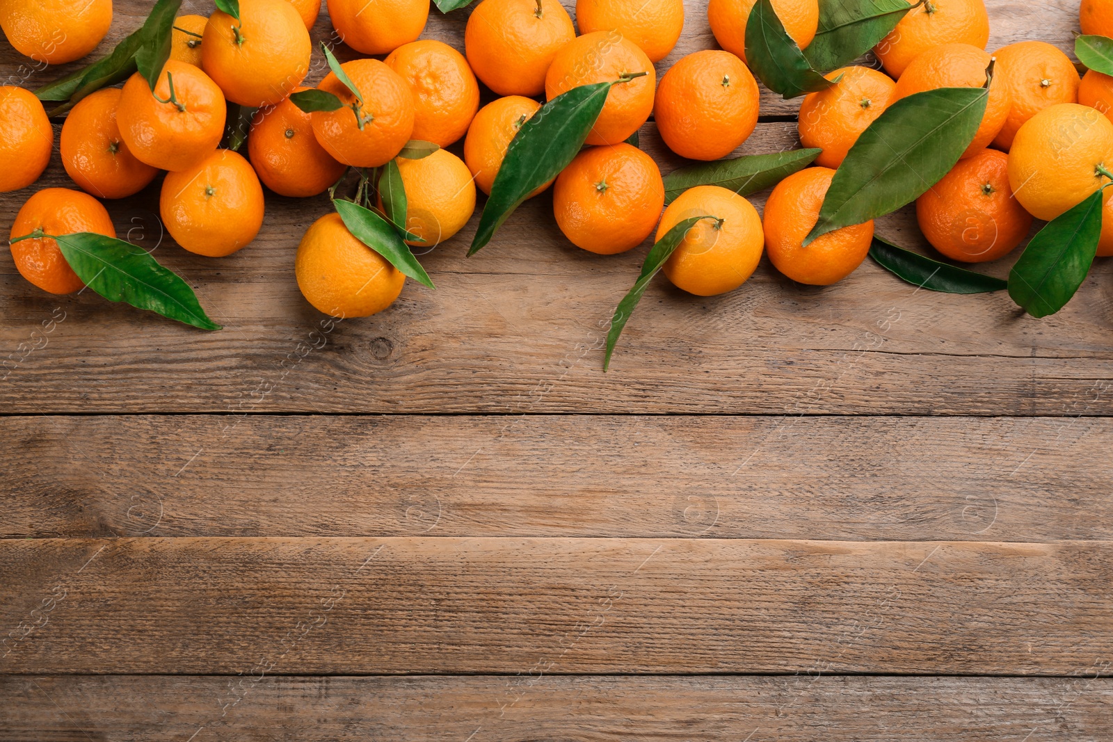 Photo of Fresh ripe tangerines with green leaves on wooden table, flat lay. Space for text