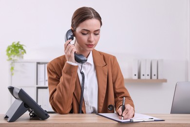 Female receptionist with clipboard talking on phone at workplace