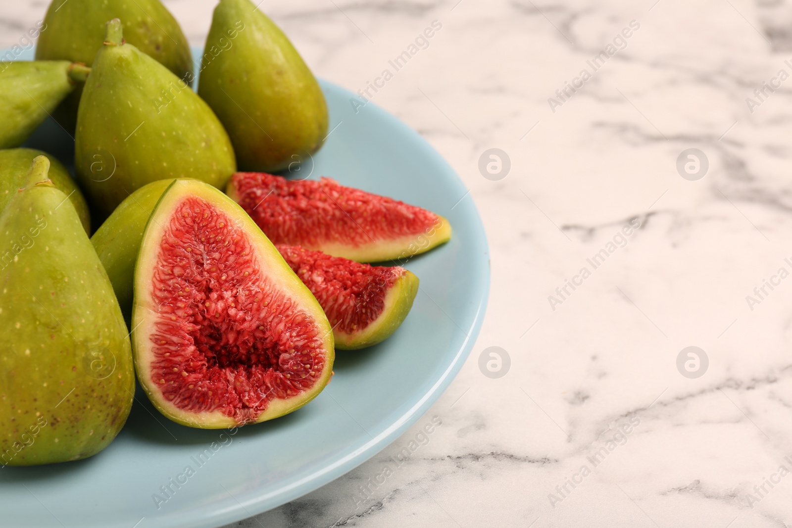 Photo of Cut and whole green figs on white marble table, closeup. Space for text
