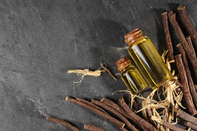 Photo of Dried sticks of licorice root and bottles with essential oil on black textured table, flat lay. Space for text