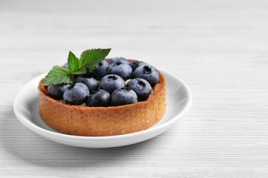 Photo of Tartlet with fresh blueberries on white wooden table, closeup and space for text. Delicious dessert