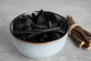 Photo of Tasty black candies and dried sticks of liquorice root on grey table
