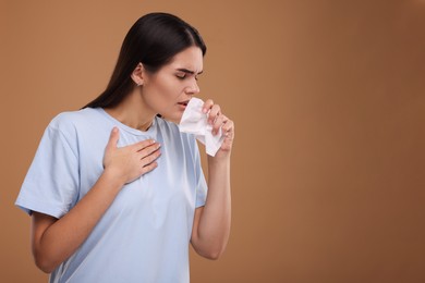Photo of Woman with tissue coughing on brown background, space for text. Cold symptoms