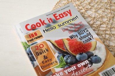 Cooking magazine and decorative mat on white wooden table, closeup