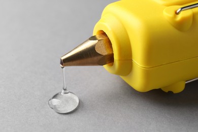 Photo of Melted glue dripping out of hot gun nozzle on grey background, closeup
