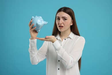 Sad woman with piggy bank on light blue background