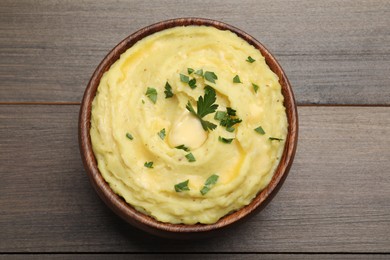 Photo of Bowl of freshly cooked mashed potatoes with parsley on wooden table, top view
