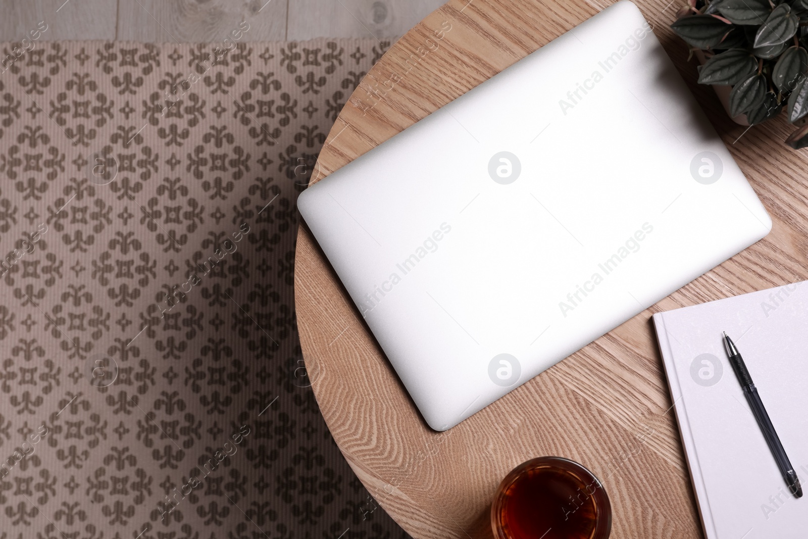 Photo of Laptop, glass of drink, houseplant and pen on wooden table in room, top view