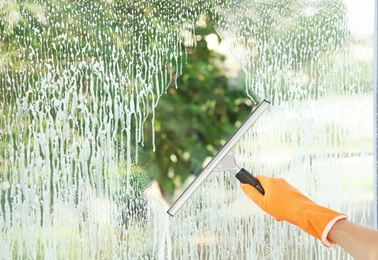 Janitor cleaning window with squeegee indoors, closeup