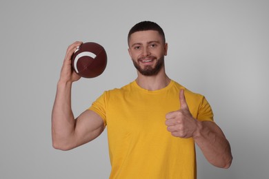 Photo of Athletic young man with American football ball showing thumb up on light grey background