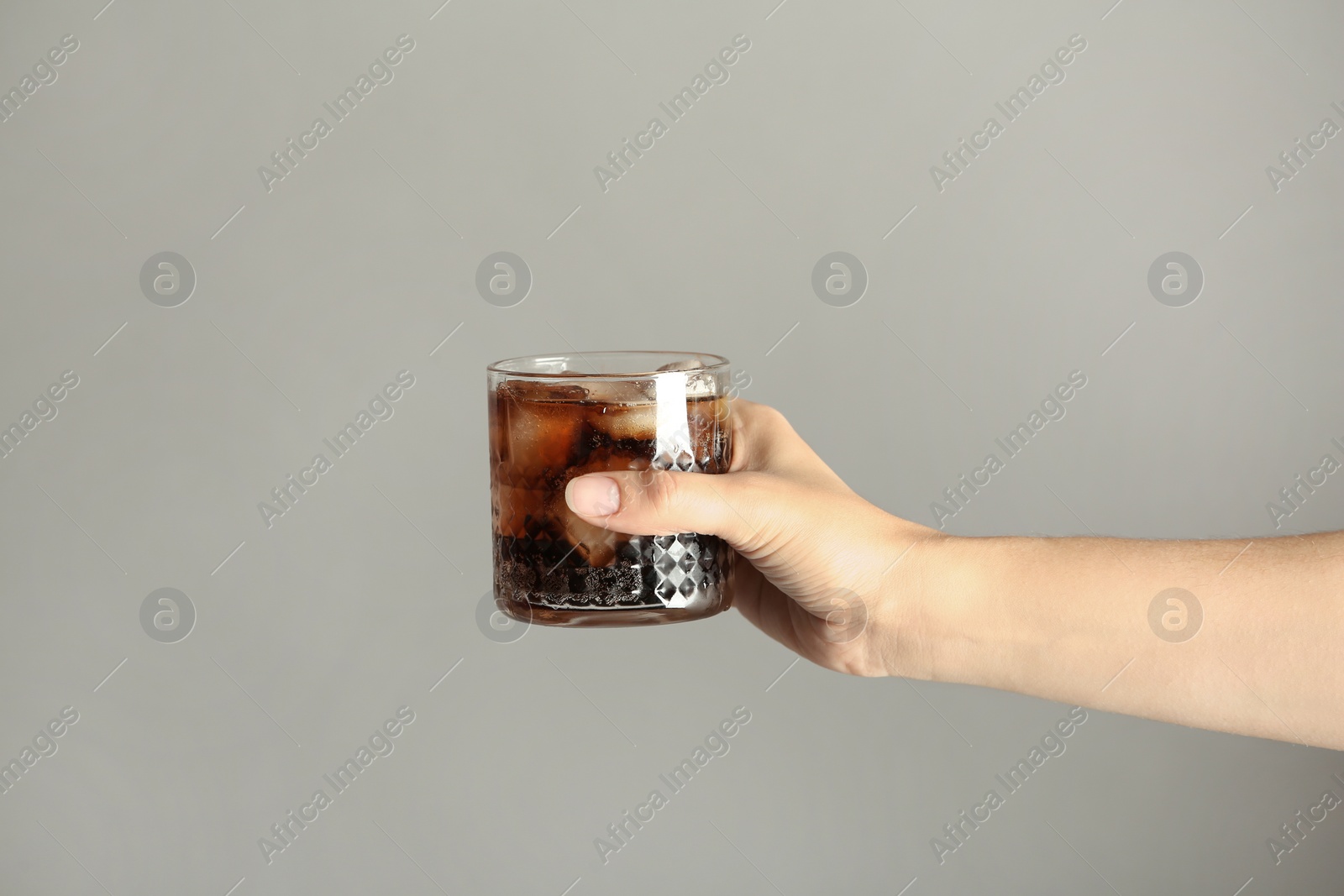 Photo of Woman holding glass of tasty refreshing cola with ice cubes on color background, closeup view