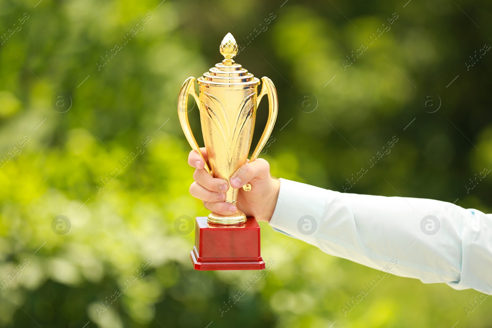 Photo of Young businessman holding gold trophy cup in green park, closeup