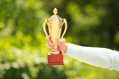 Young businessman holding gold trophy cup in green park, closeup