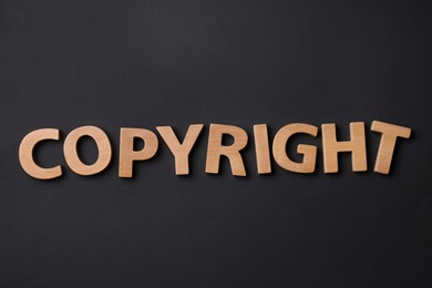Photo of Word Copyright made of wooden letters on black background, flat lay. Plagiarism concept