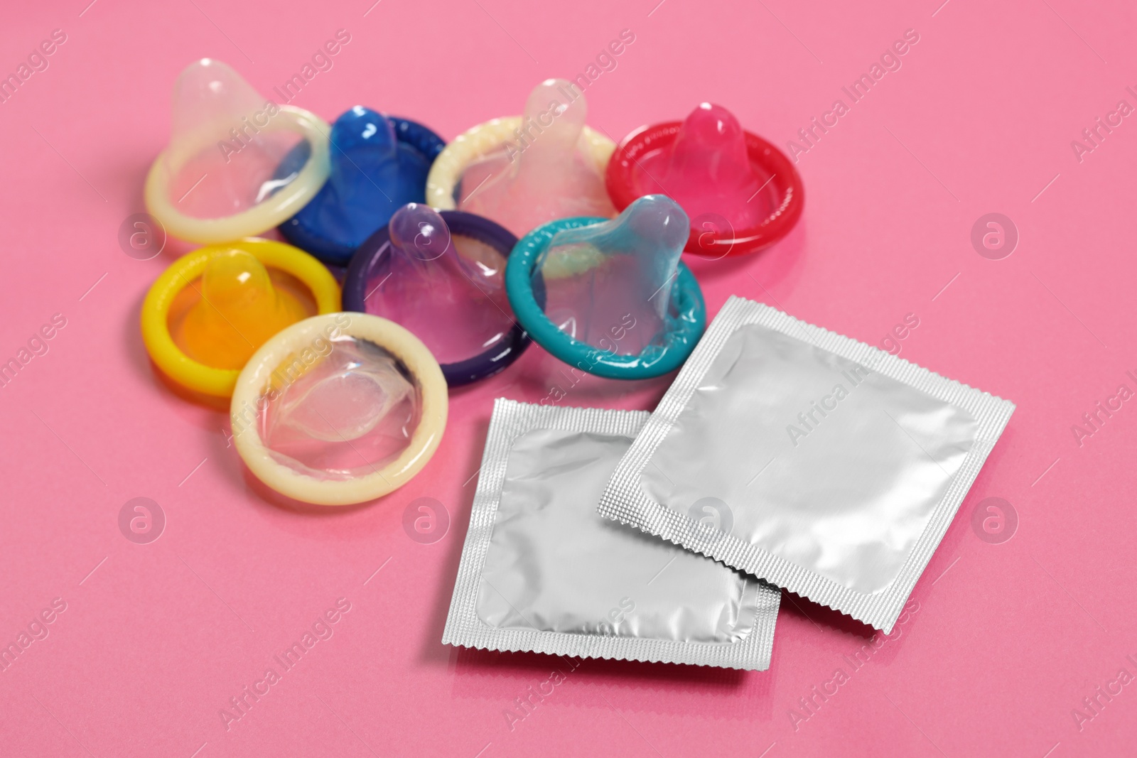 Photo of Unpacked condoms and packages on pink background. Safe sex