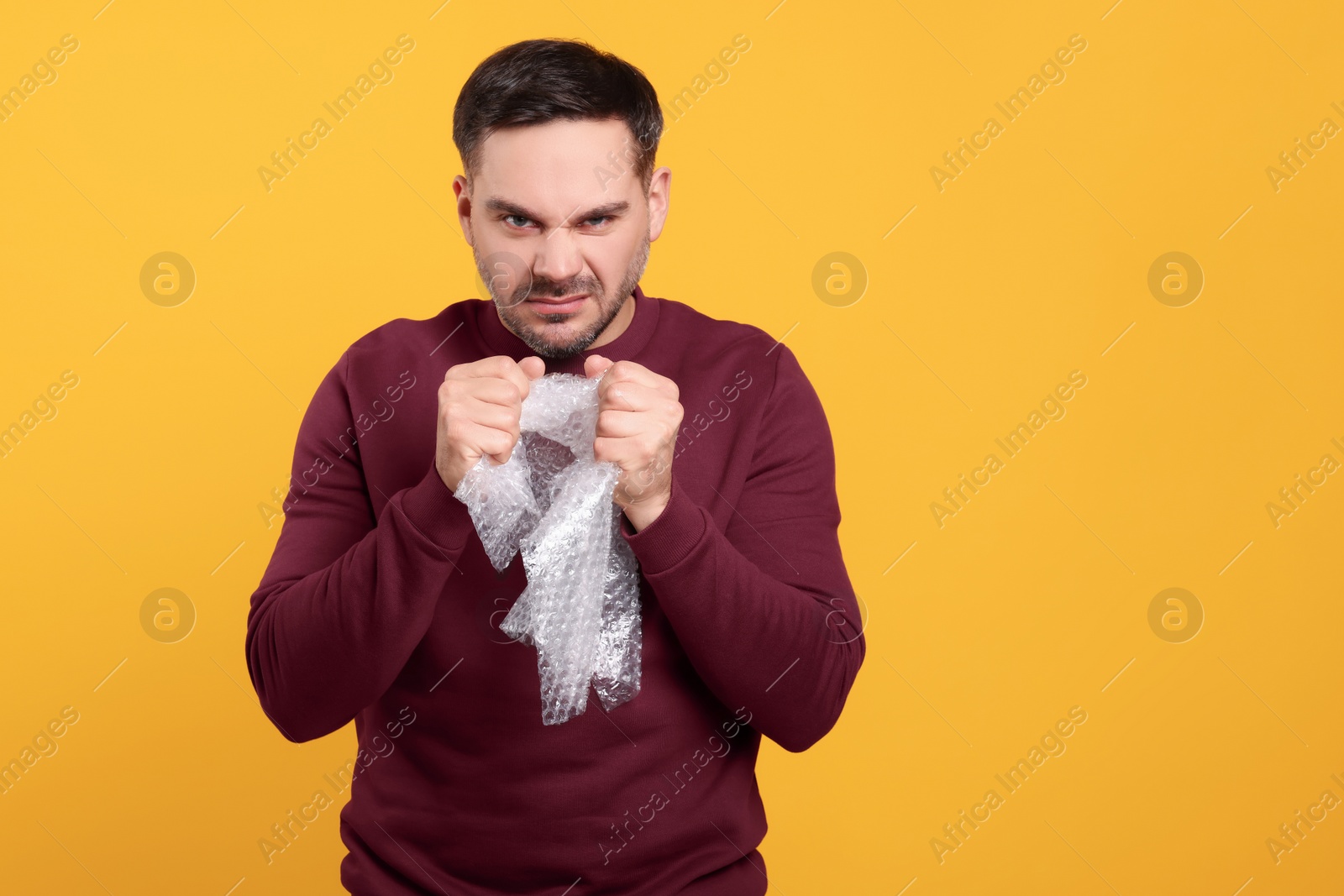 Photo of Emotional asian man with bubble wrap on orange background. Space for text