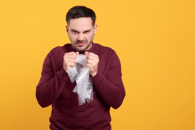 Photo of Emotional asian man with bubble wrap on orange background. Space for text