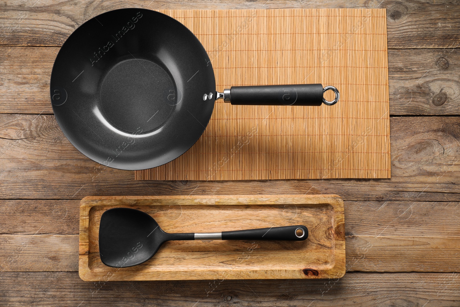 Photo of Black metal wok and spatula on wooden table, top view