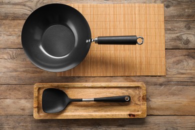 Black metal wok and spatula on wooden table, top view