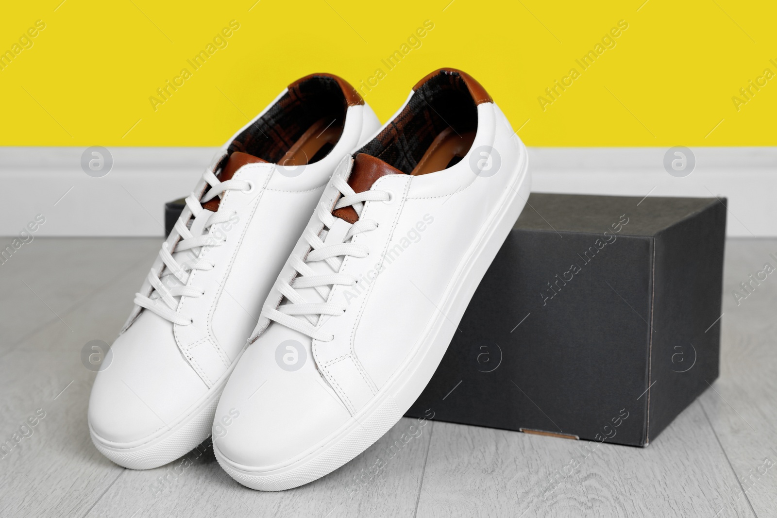 Photo of Pair of stylish sports shoes near cardboard box on floor indoors