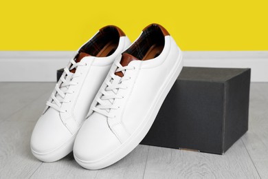 Photo of Pair of stylish sports shoes near cardboard box on floor indoors