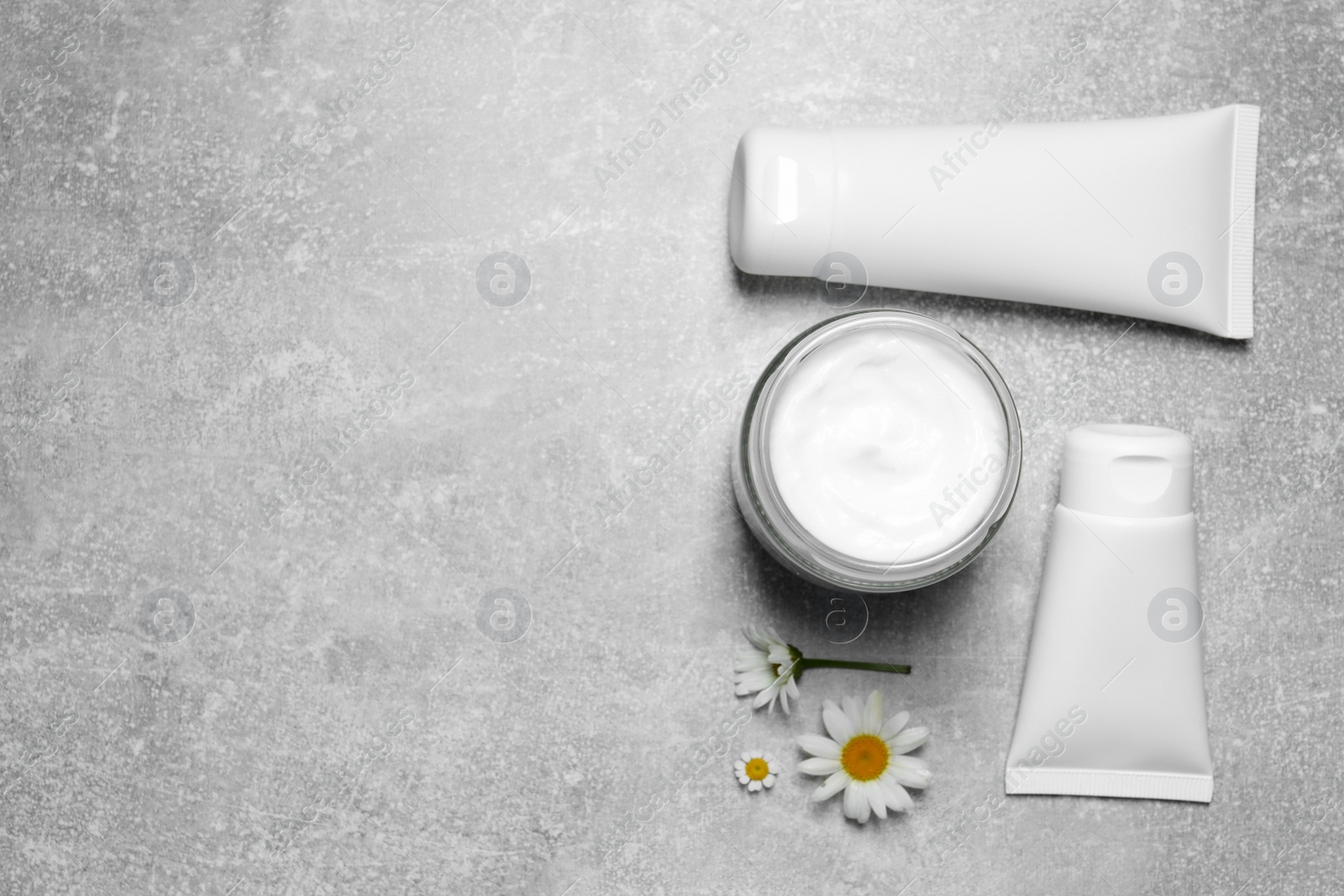 Photo of Different hand care cosmetic products and chamomiles on light grey table, flat lay. Space for text