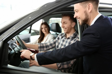 Photo of Salesman consulting young couple in auto at dealership. Buying new car