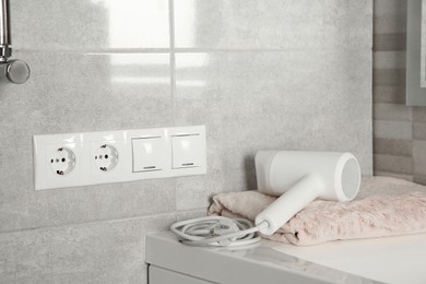 Power sockets, light switches on wall near table with hairdryer and towel indoors