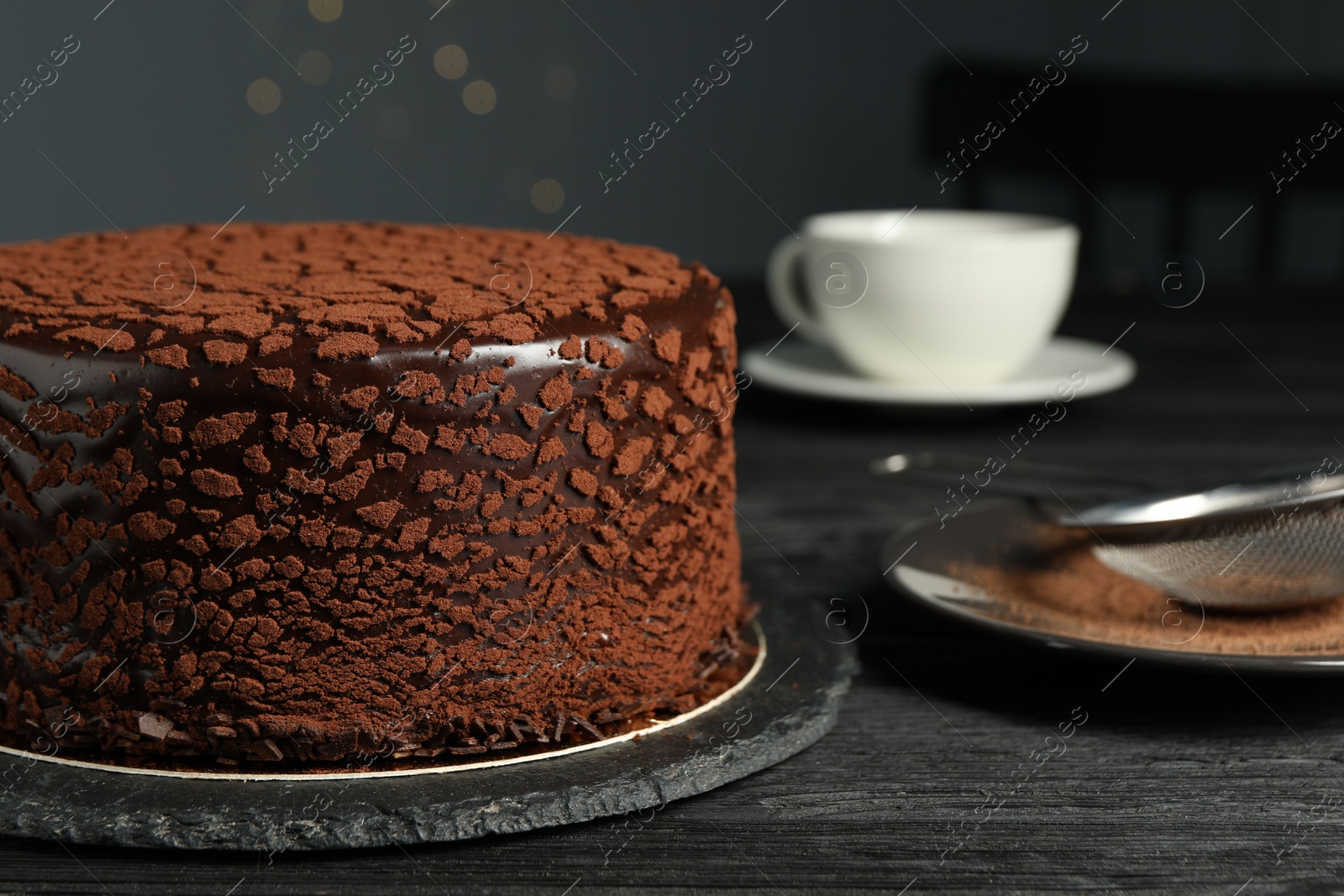 Photo of Delicious chocolate truffle cake and cocoa powder on black wooden table, closeup