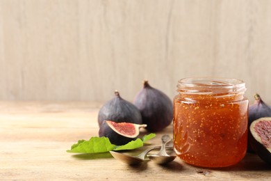 Glass jar with tasty sweet jam, spoons and fresh figs on wooden table. Space for text