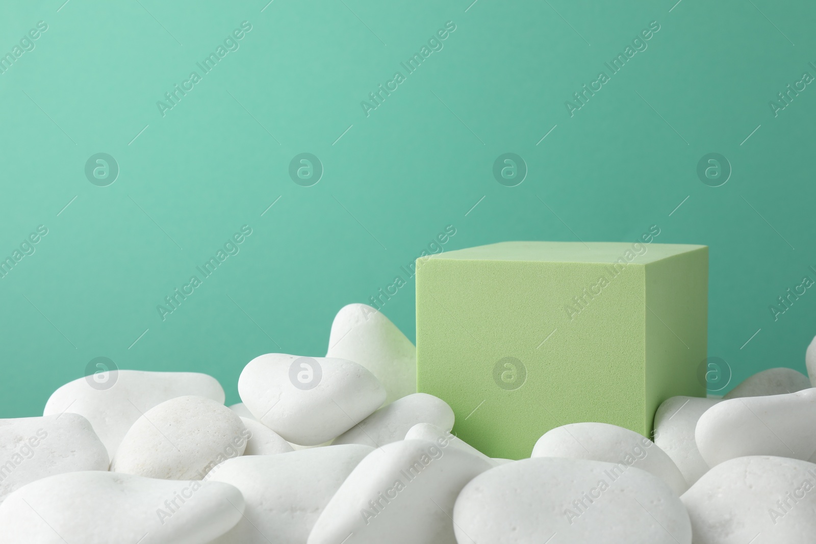 Photo of Presentation for product. Light green cube podium and white pebbles on color background. Space for text