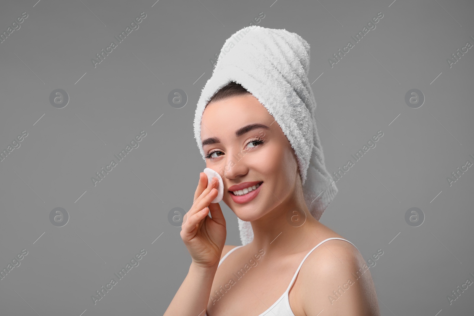 Photo of Beautiful woman in terry towel removing makeup with cotton pad on gray background