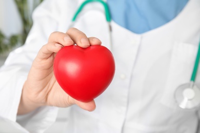 Doctor holding red heart, closeup view with space for text. Cardiology concept