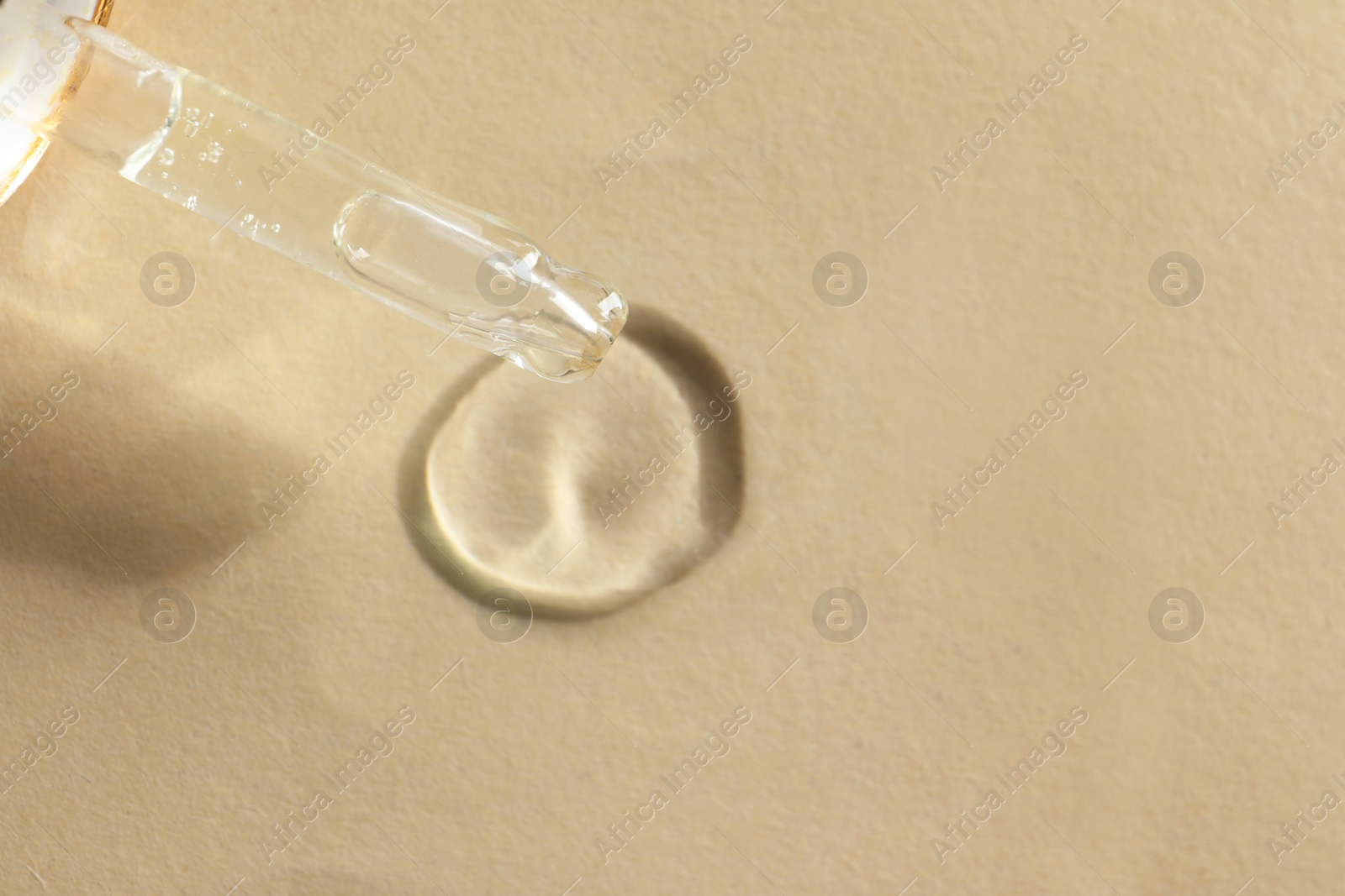 Photo of Dripping cosmetic oil from pipette onto beige background, closeup. Space for text