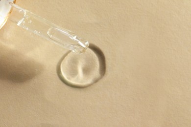 Dripping cosmetic oil from pipette onto beige background, closeup. Space for text