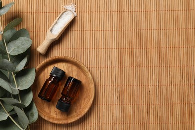 Photo of Aromatherapy products. Bottles of essential oil, sea salt and eucalyptus branches on bamboo mat, flat lay. Space for text