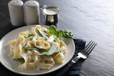 Photo of Delicious pasta with green peas and creamy sauce on black table