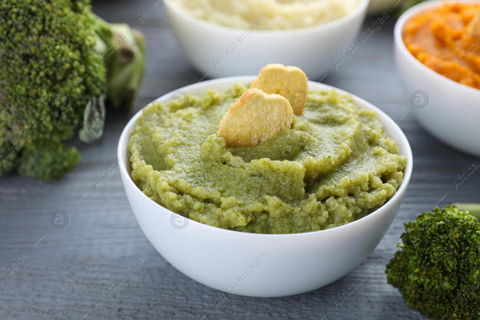 Photo of Bowl with tasty green puree and ingredients on light blue wooden table, closeup