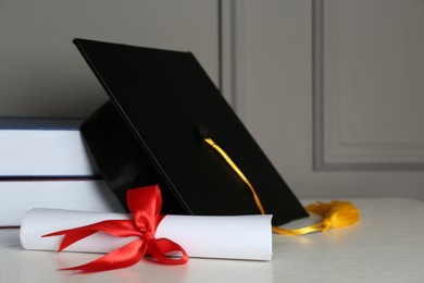 Graduation hat, books and diploma on white table near grey wall, space for text