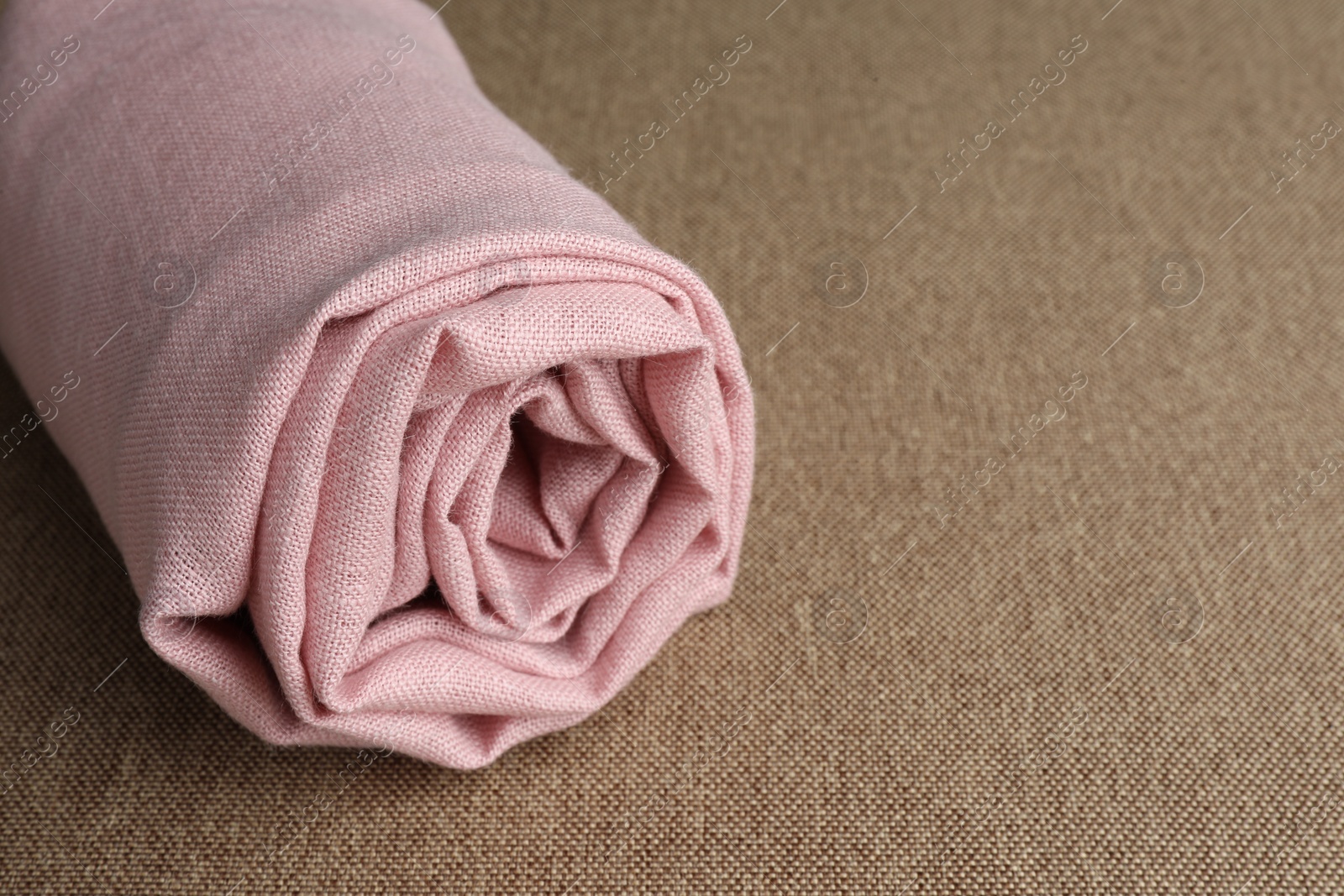 Photo of Rolled pink fabric on brown cloth, closeup. Space for text